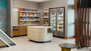 Ein modernes Interieur mit einer zentralen Theke, Regalen voller Snacks, einem Kühlschrank und einem kleinen Tisch.