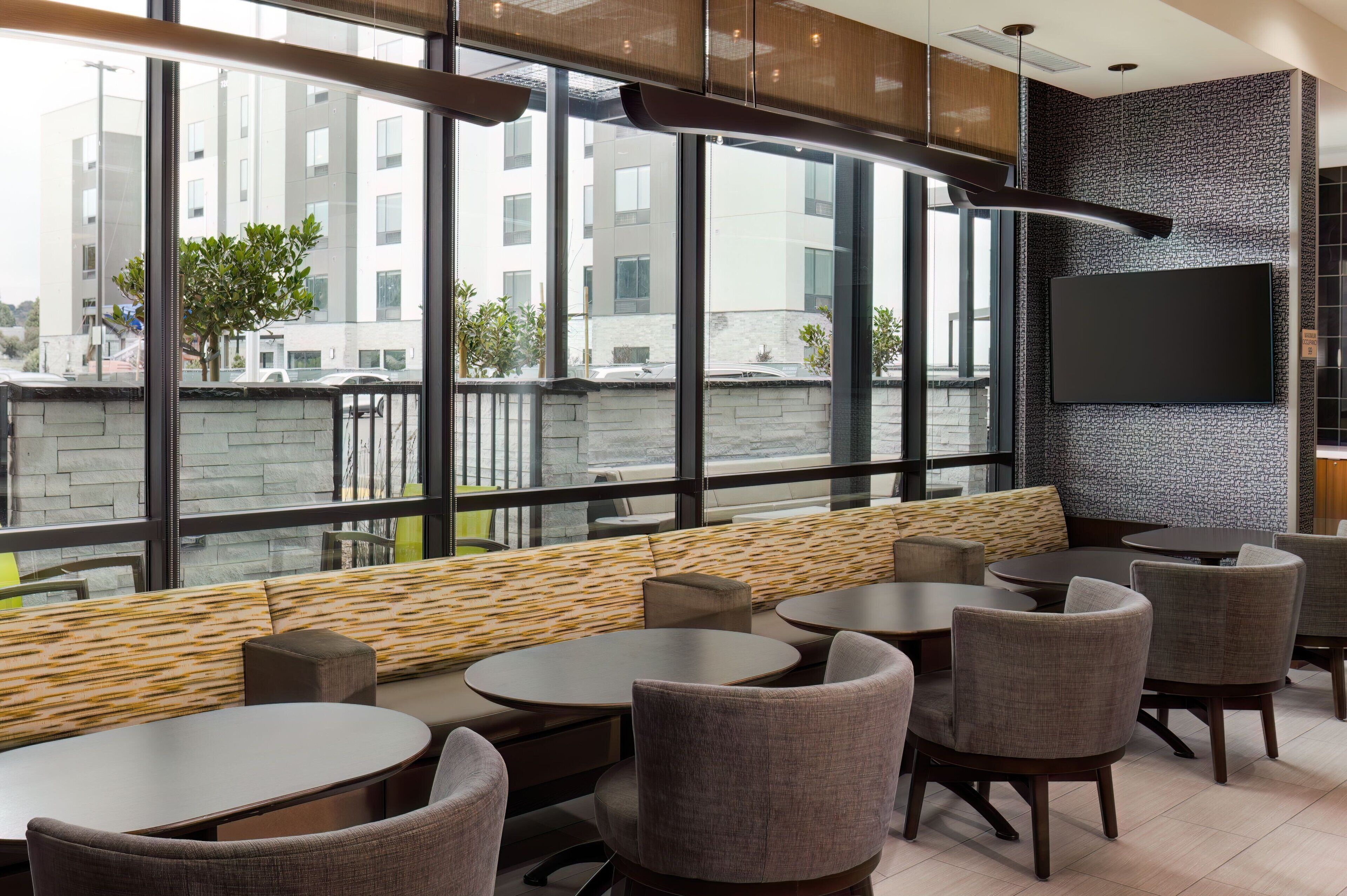 A modern lounge area with large windows, comfortable seating, and a flat-screen TV.