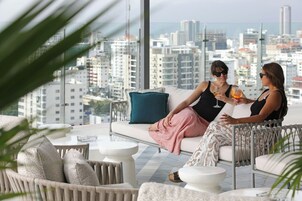 A modern lounge area with a city view, furnished with sofas, chairs, and small tables.
