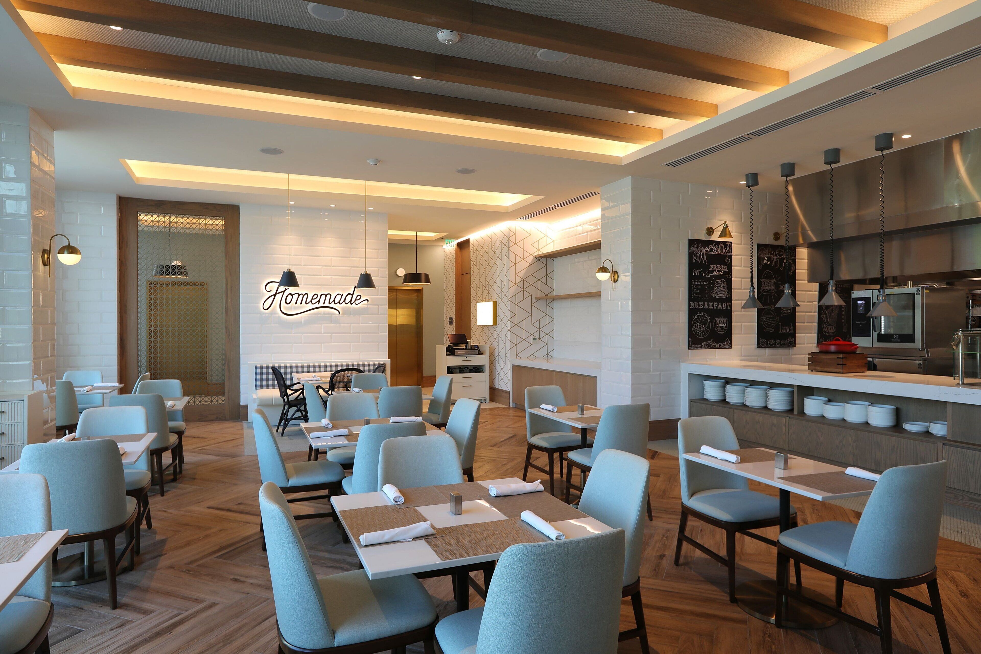 A modern restaurant with a central bar area, multiple seating options, and a visible kitchen.