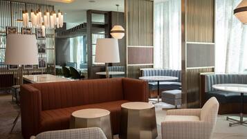 A modern hotel lobby with a brown leather sofa, round tables, and a seating area with blue upholstered chairs.