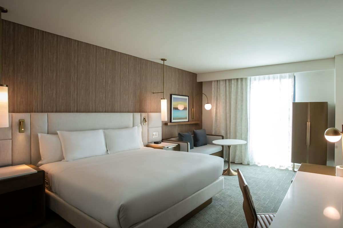 Habitació d'hotel amb un llit gran, un taulell petit, una cadira, una taula rodona i un armari.