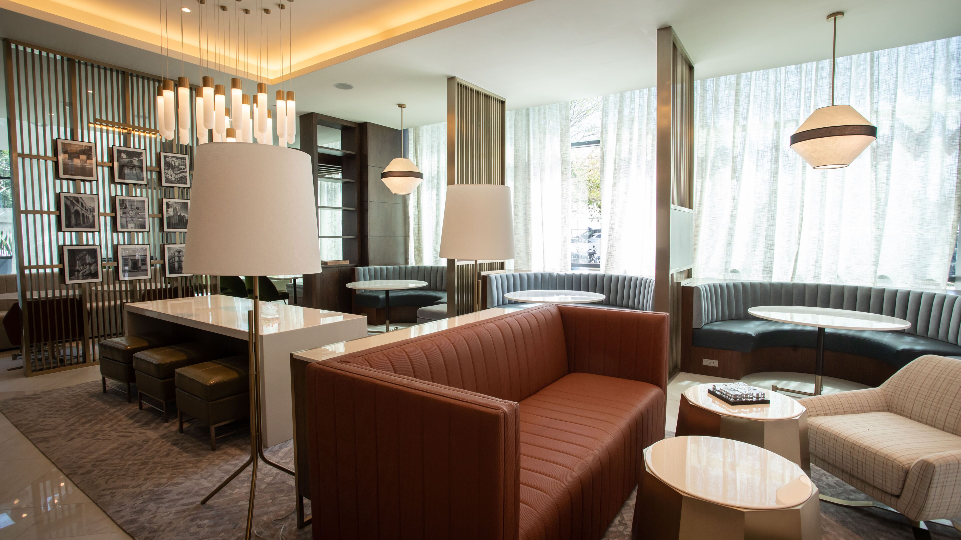 Un moderno vestíbulo de hotel con una zona de estar central, un bar y un amplio ventanal que proporciona luz natural.