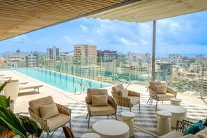 Zona de piscina en la azotea con sillones reclinables y vista a la ciudad.