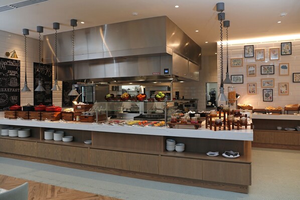 A modern breakfast bar with a stainless steel range hood, a variety of breakfast items, and artwork on the walls.