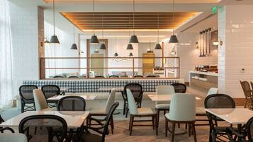 Interno di un ristorante moderno con sedute a cabina a scacchi, diversi tavoli e lampade a sospensione.