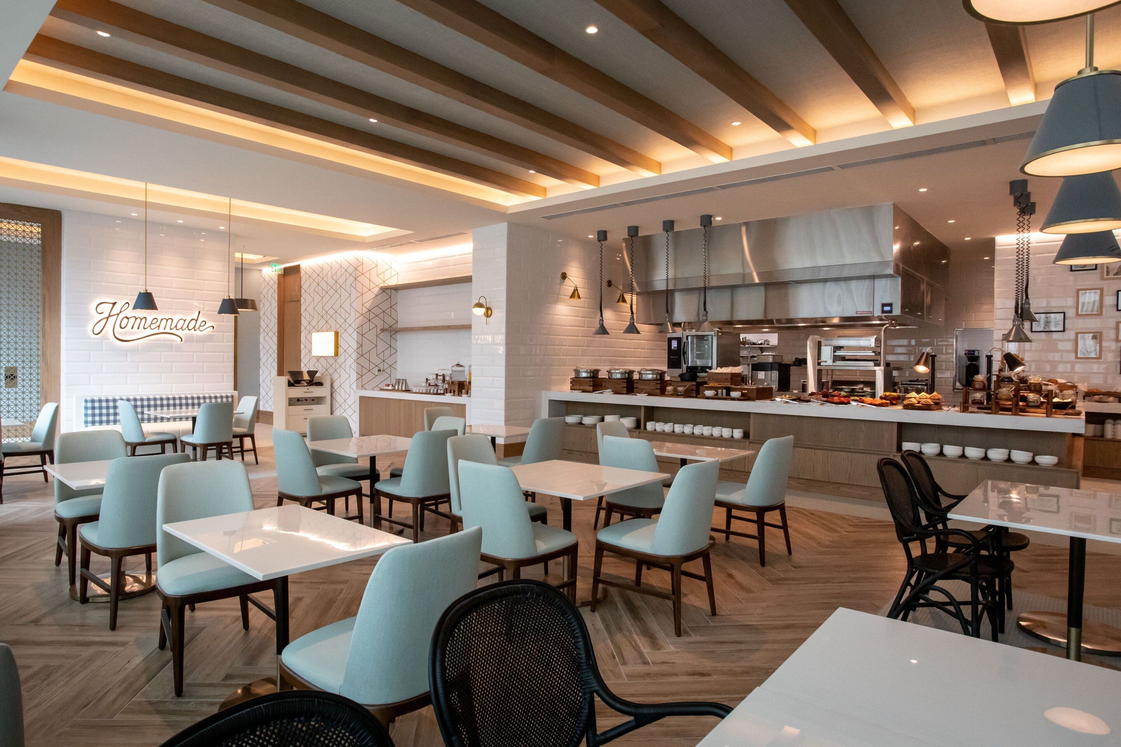 A modern restaurant with light blue chairs and white tables, a visible kitchen area, and a sign that reads "Homemade."