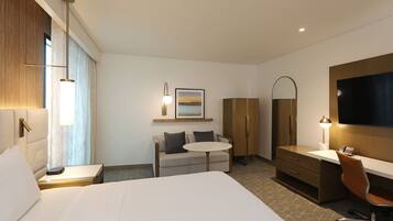 Hotelkamer met een groot bed, een bureau met stoel, een klein rond tafeltje, een bank, een kledingkast, een televisie en een schilderij aan de muur.