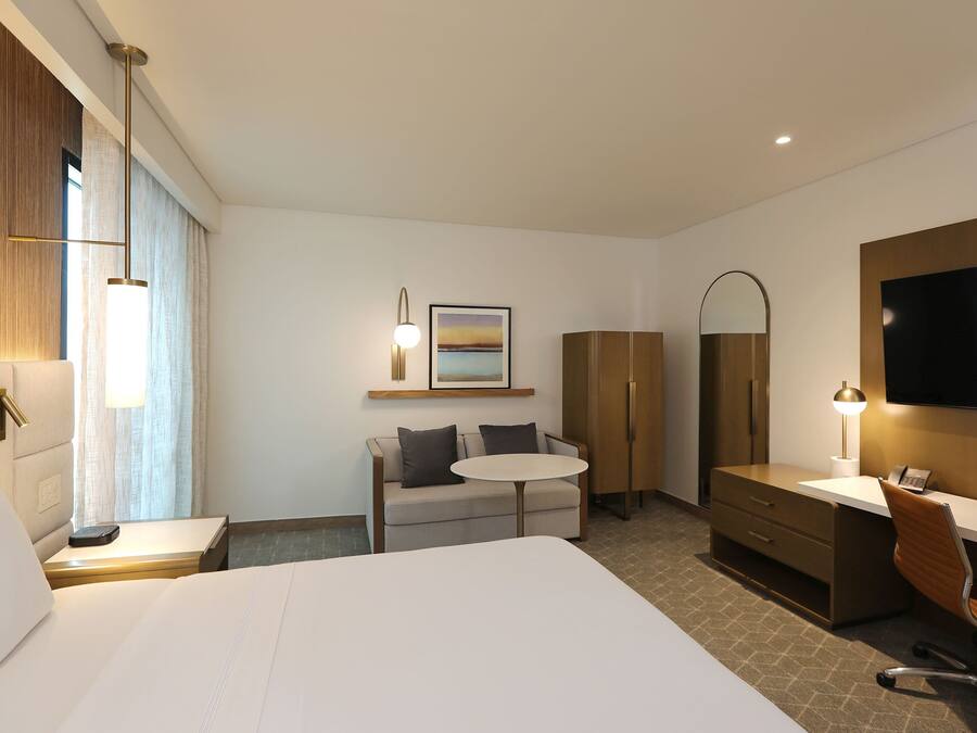 Hotelkamer met een groot bed, een bureau met stoel, een klein rond tafeltje, een bank, een kledingkast, een televisie en een schilderij aan de muur.