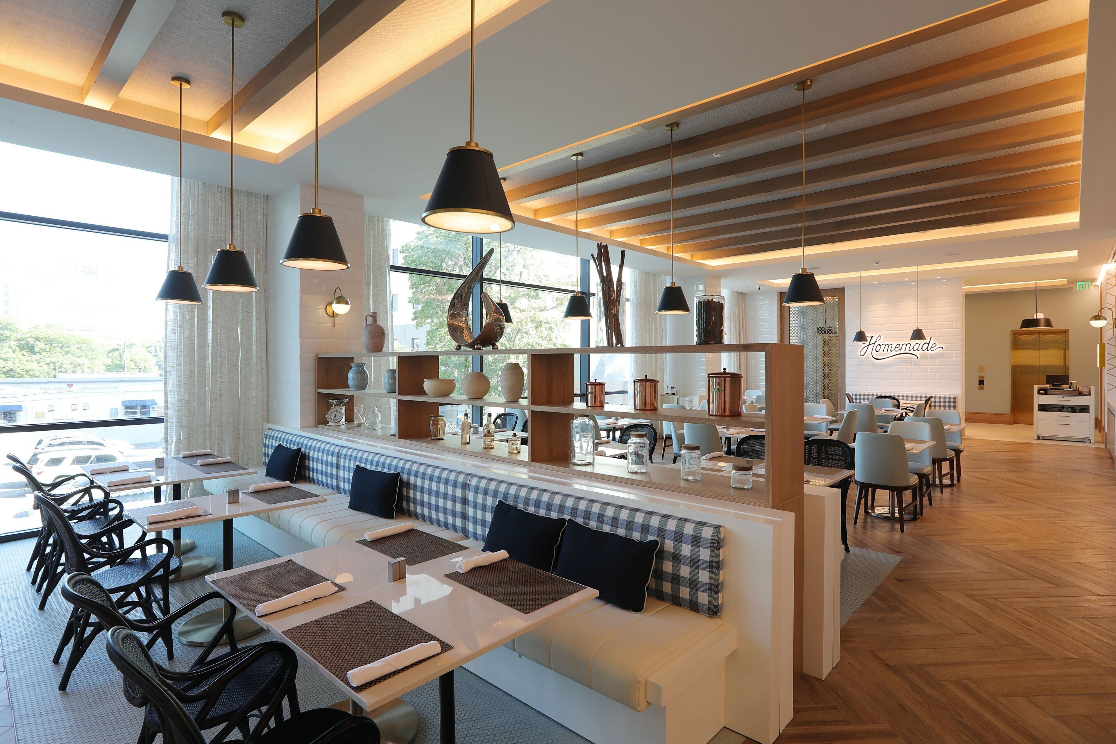 Un restaurante moderno con una barra larga, varias mesas y una zona de estar con un banco a cuadros.