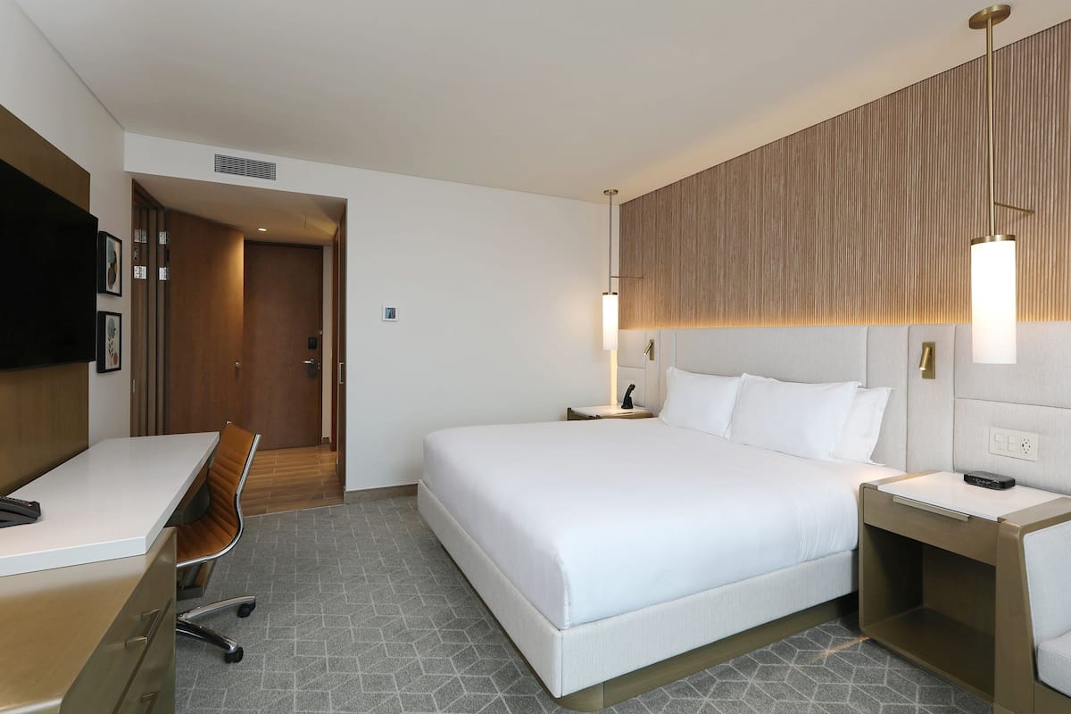 Habitació d'hotel amb un llit, una escriptori, una cadira, una tauleta de nit i un televisor.