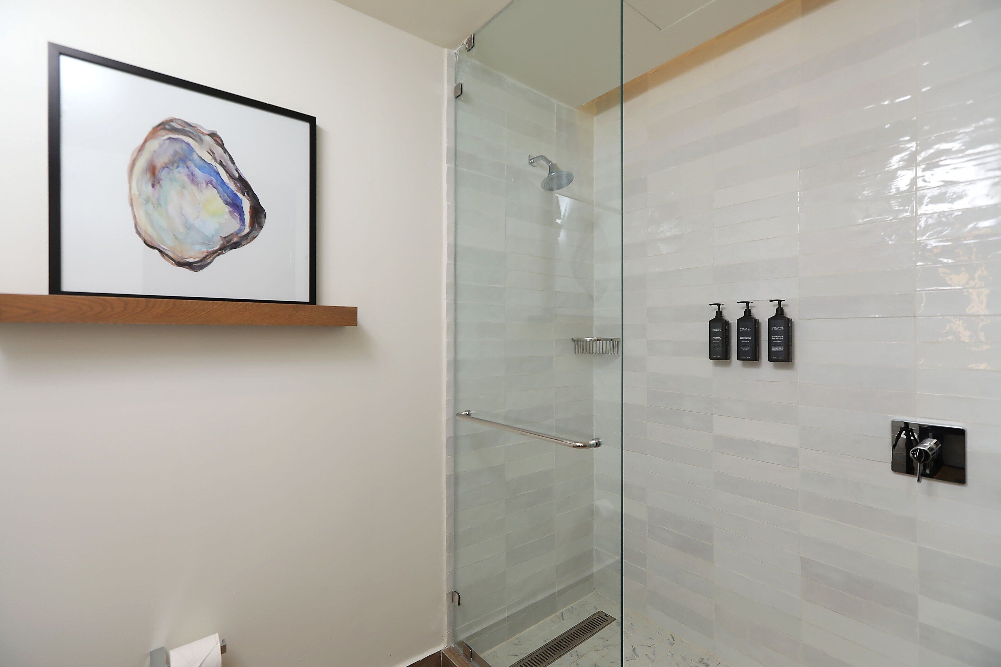 Un baño moderno con cabina de ducha de vidrio, un cuadro abstracto enmarcado en la pared y artículos de tocador sobre una estantería.