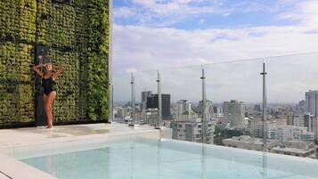 A rooftop infinity pool with a city view, a glass railing, and a green wall.