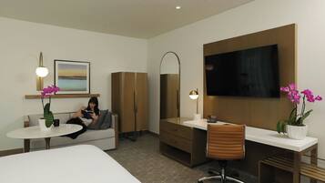 Een hotelkamer met een bed, een bureau, een stoel, een televisie, een bank, een salontafel en twee potplanten.