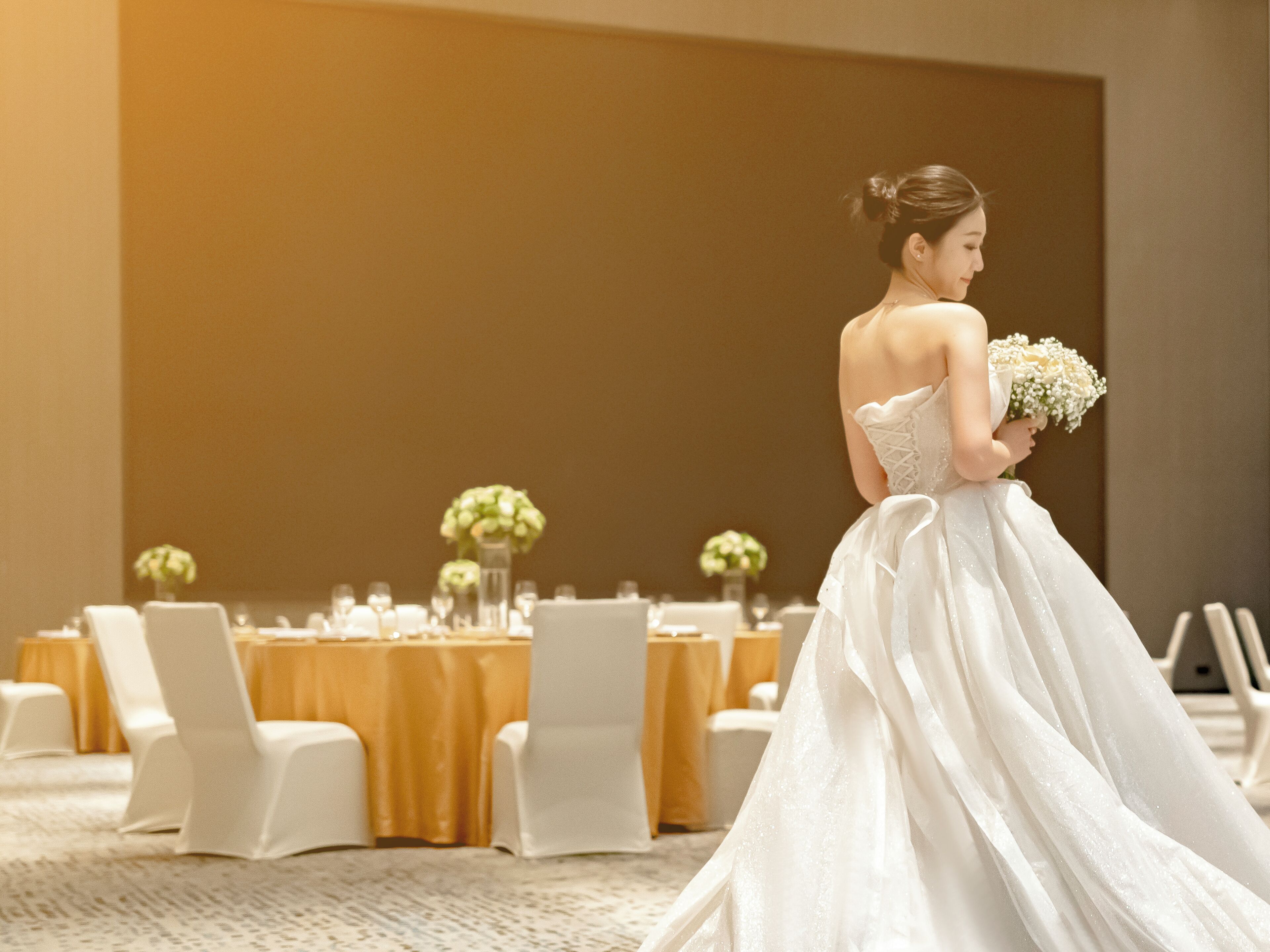 A wedding venue with round tables, white chairs, and floral centerpieces.