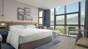 Habitación de hotel moderna con una cama grande, un escritorio y vistas a montañas a través de amplios ventanales.