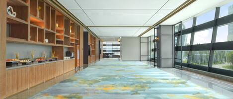 A spacious corridor with a patterned carpet, wooden shelving units, and large windows offering views of the outside.