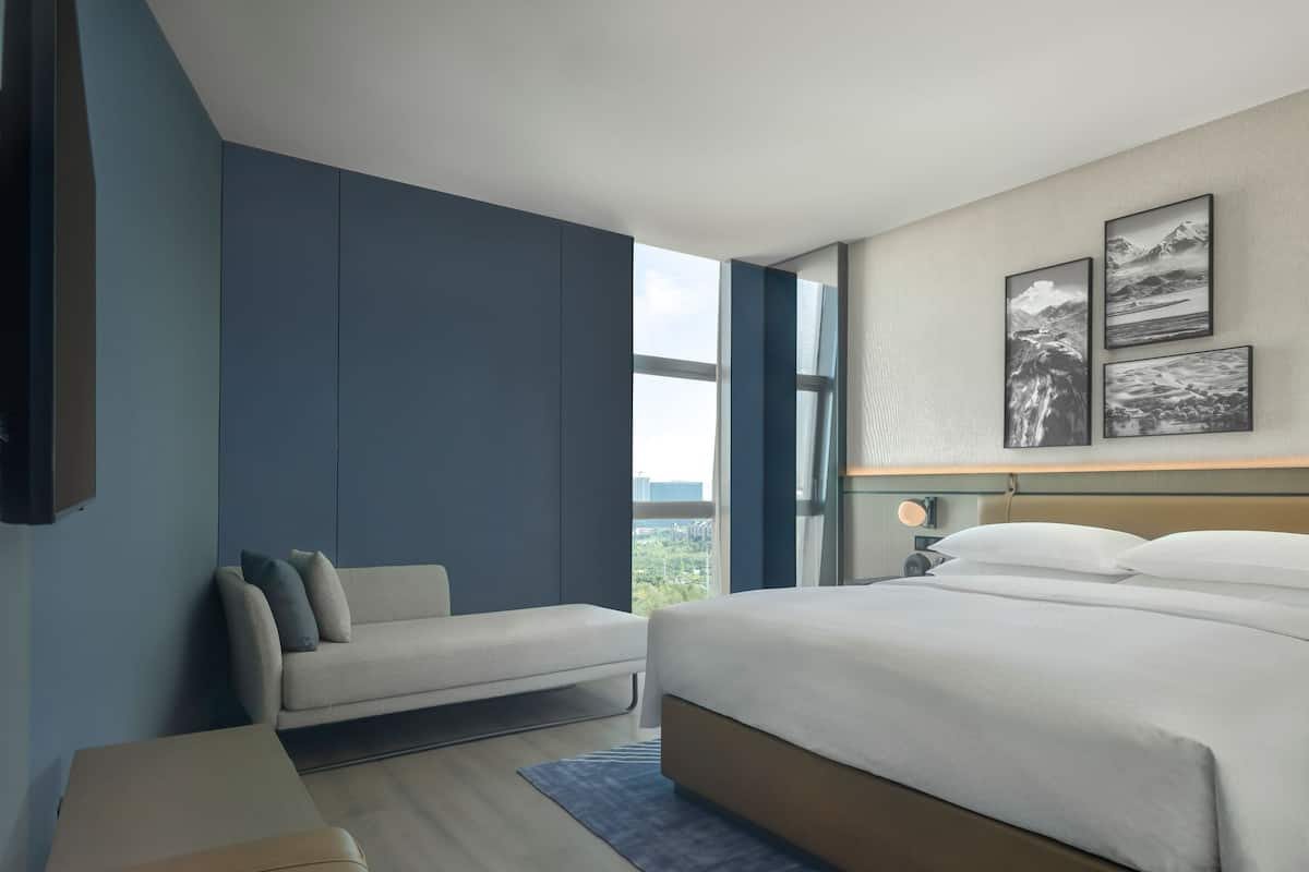 A modern hotel room with a large bed, a sofa, and a view of the outdoors.