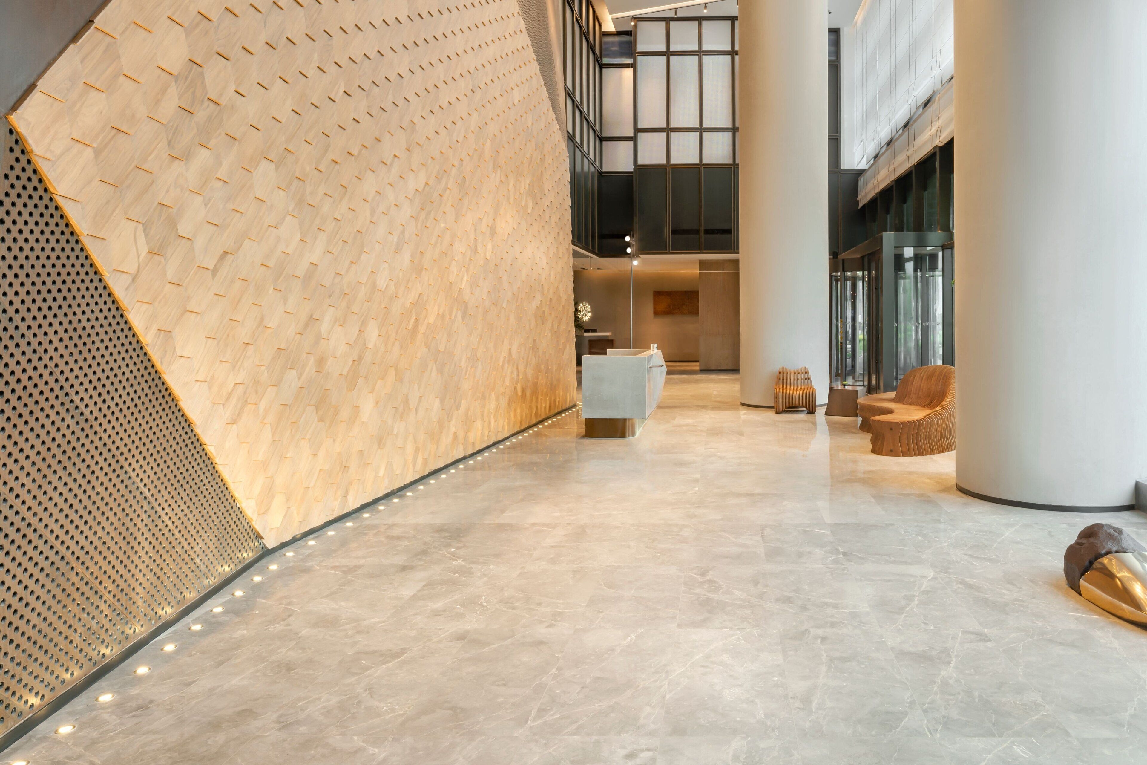 A modern lobby with a polished marble floor, a wooden textured wall, and contemporary furniture.