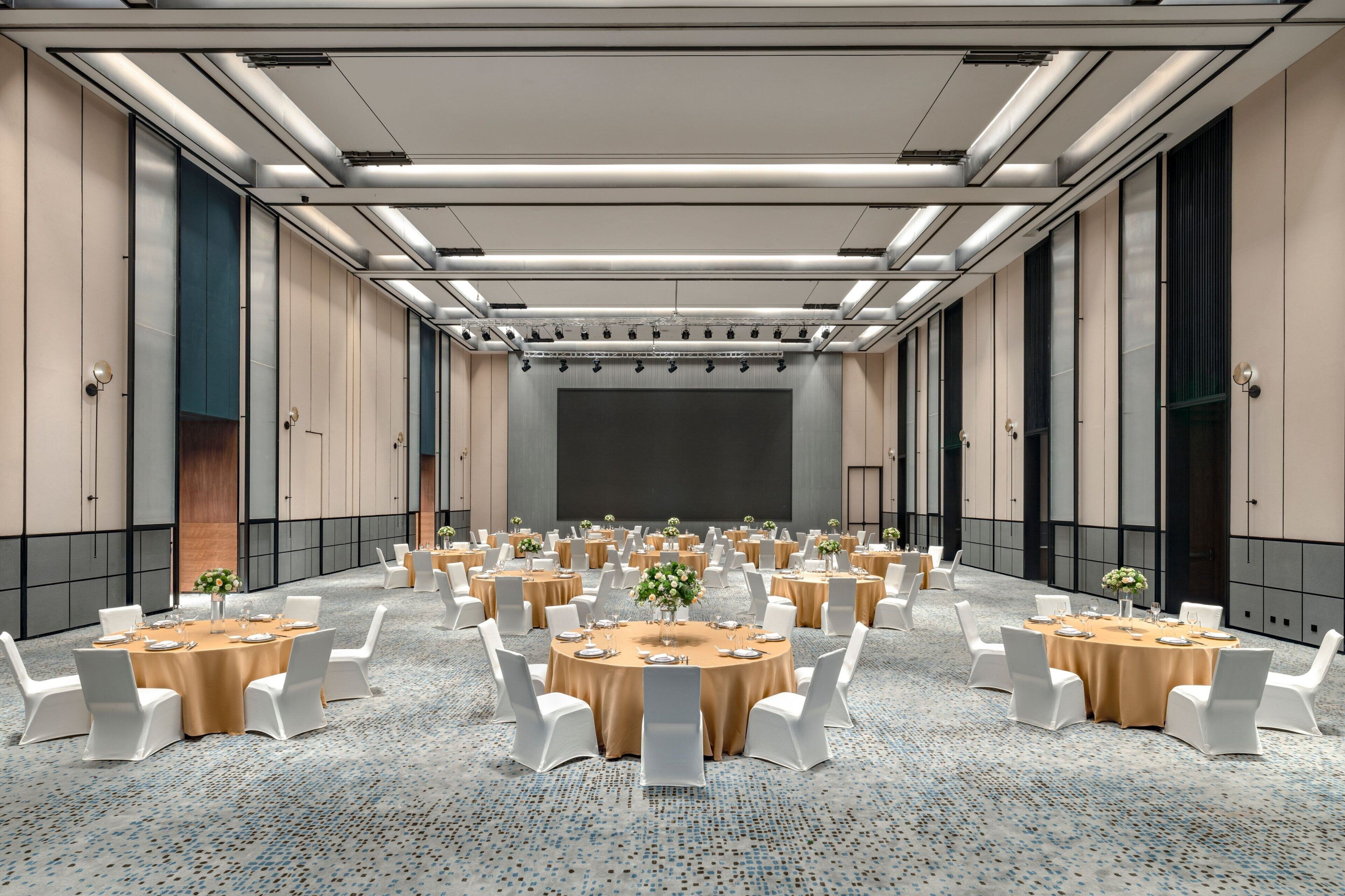 A conference room with multiple round tables, white chairs, and a carpeted floor.