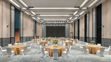 A conference room with multiple round tables, white chairs, and a carpeted floor.