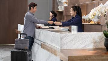 Un mostrador de recepción de hotel con encimeras de mármol, una maleta negra y un florero con flores blancas.
