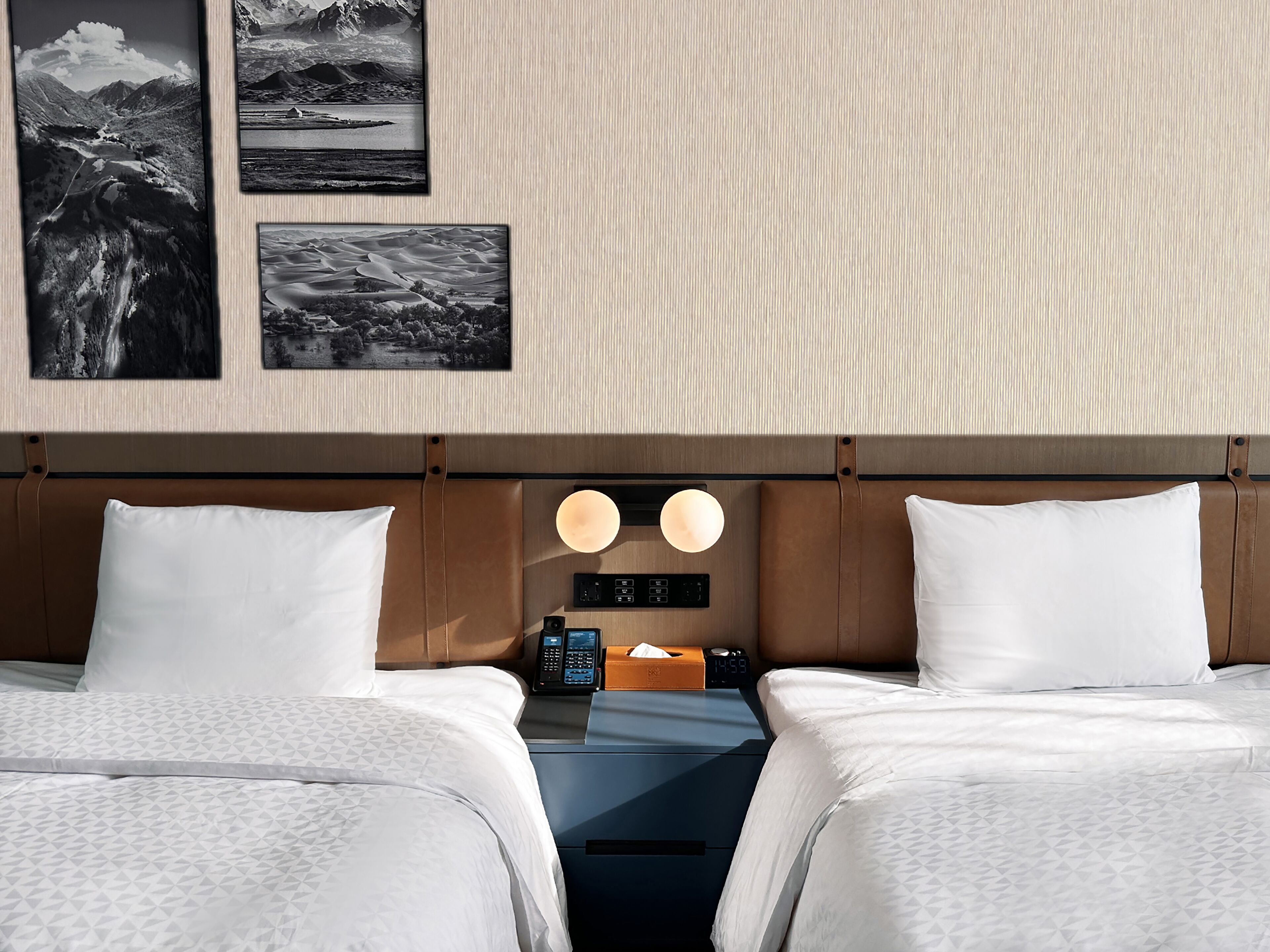 A hotel room with two beds, a wooden headboard, a bedside table with a lamp, and a wall-mounted phone.