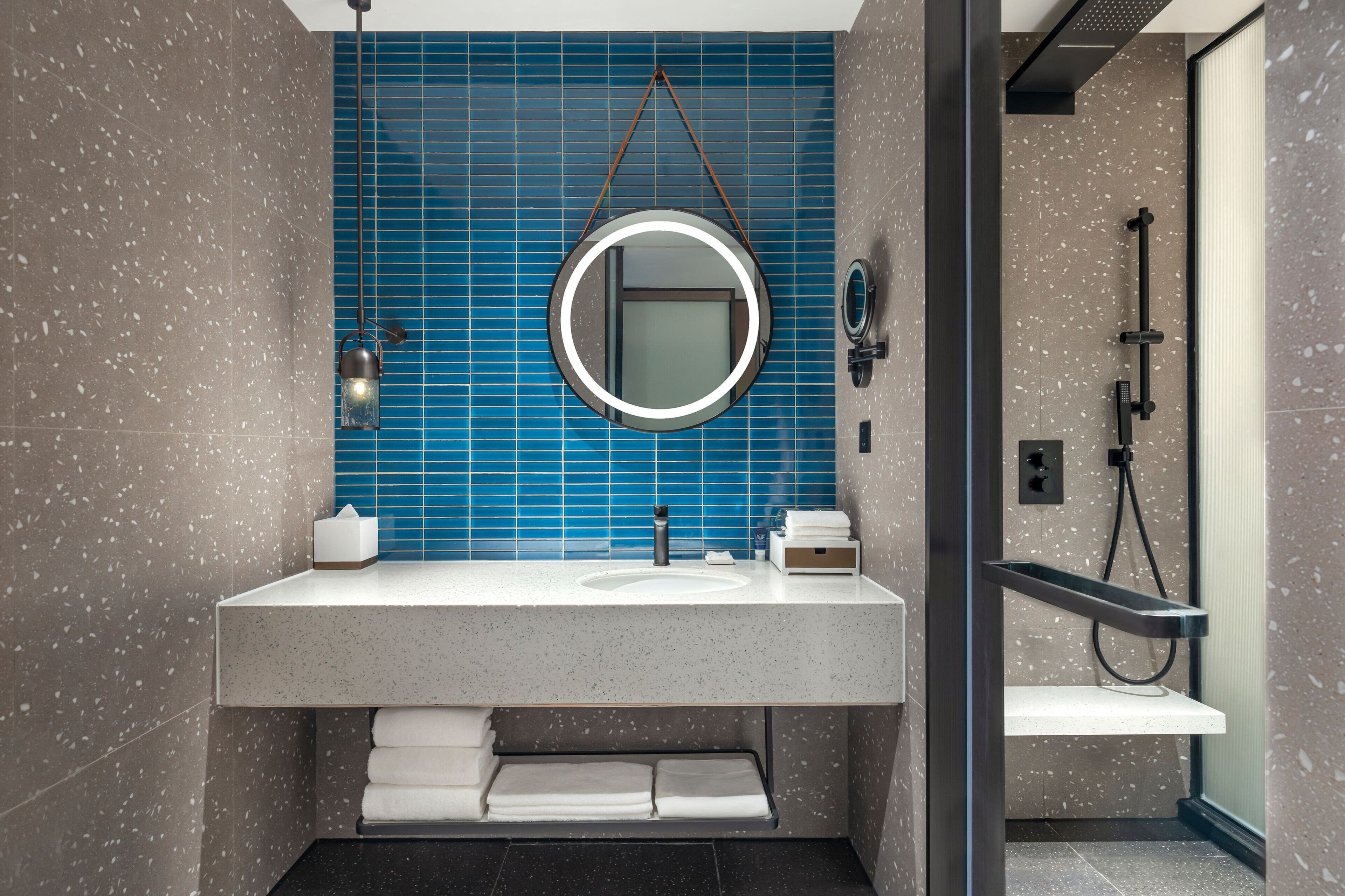 A modern bathroom with a large sink, a round mirror, and a shower area.