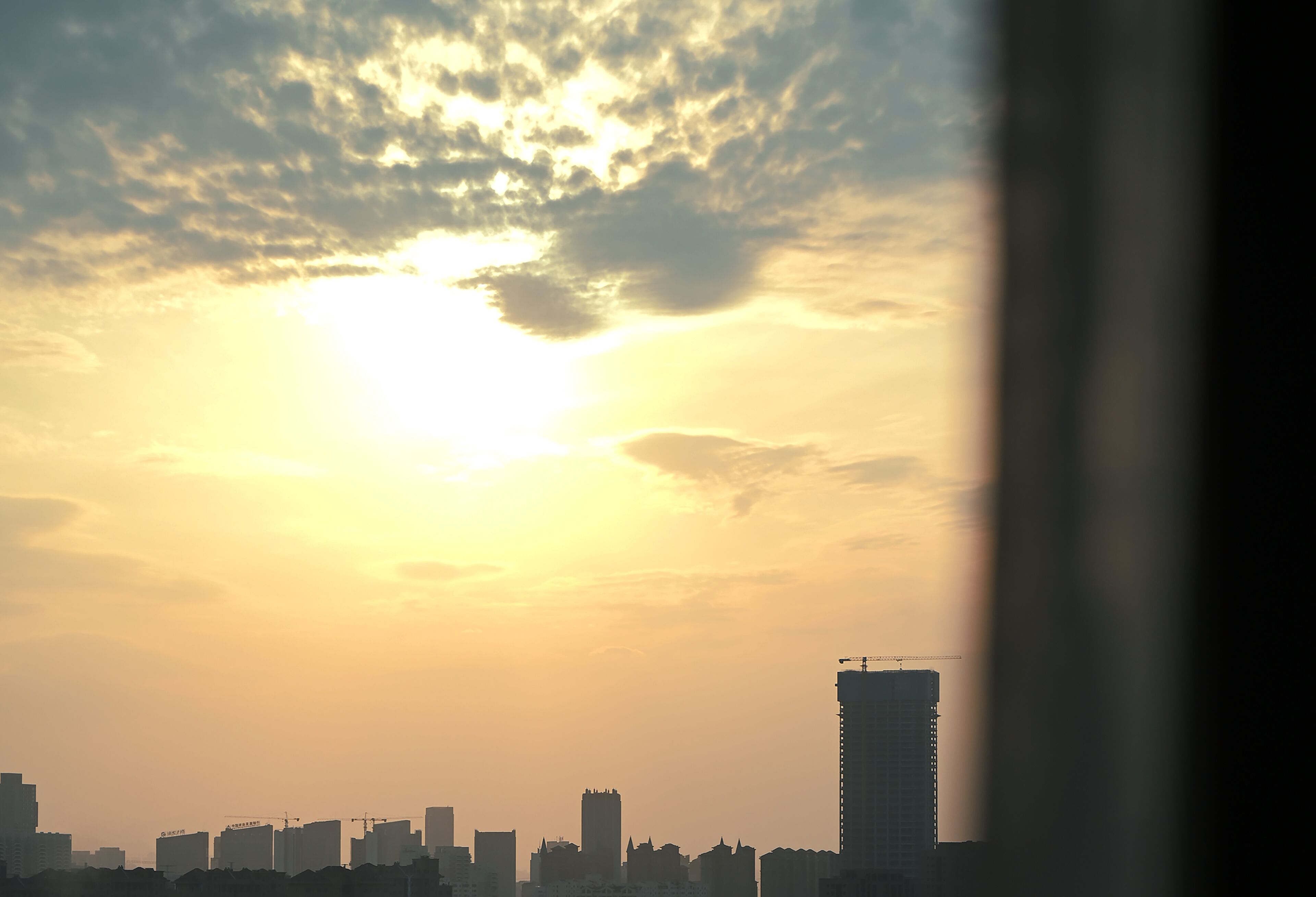 A city skyline at sunset with silhouettes of buildings and a construction crane.