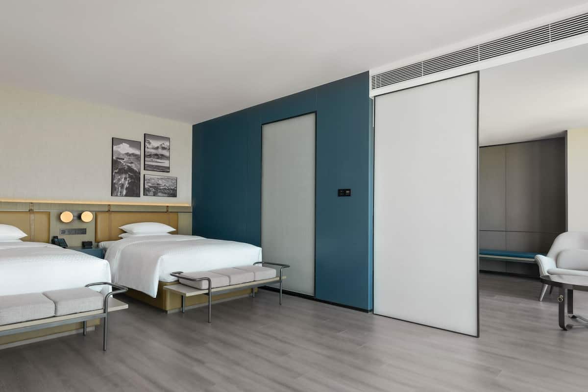 A modern hotel room with two beds, a desk, and a chair.
