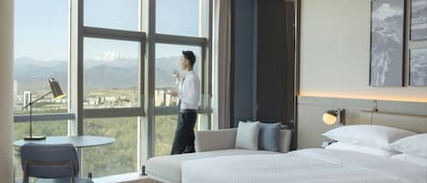 Habitación de hotel moderna con una cama grande, un escritorio y una silla. Se ve una vista de montañas a través de la ventana.