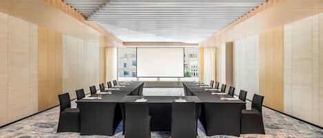 A conference room with a long table, black chairs, and a large screen at the front.
