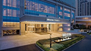 Un hotel moderno con una entrada destacada, ventanas amplias y un área ajardinada con fuente.