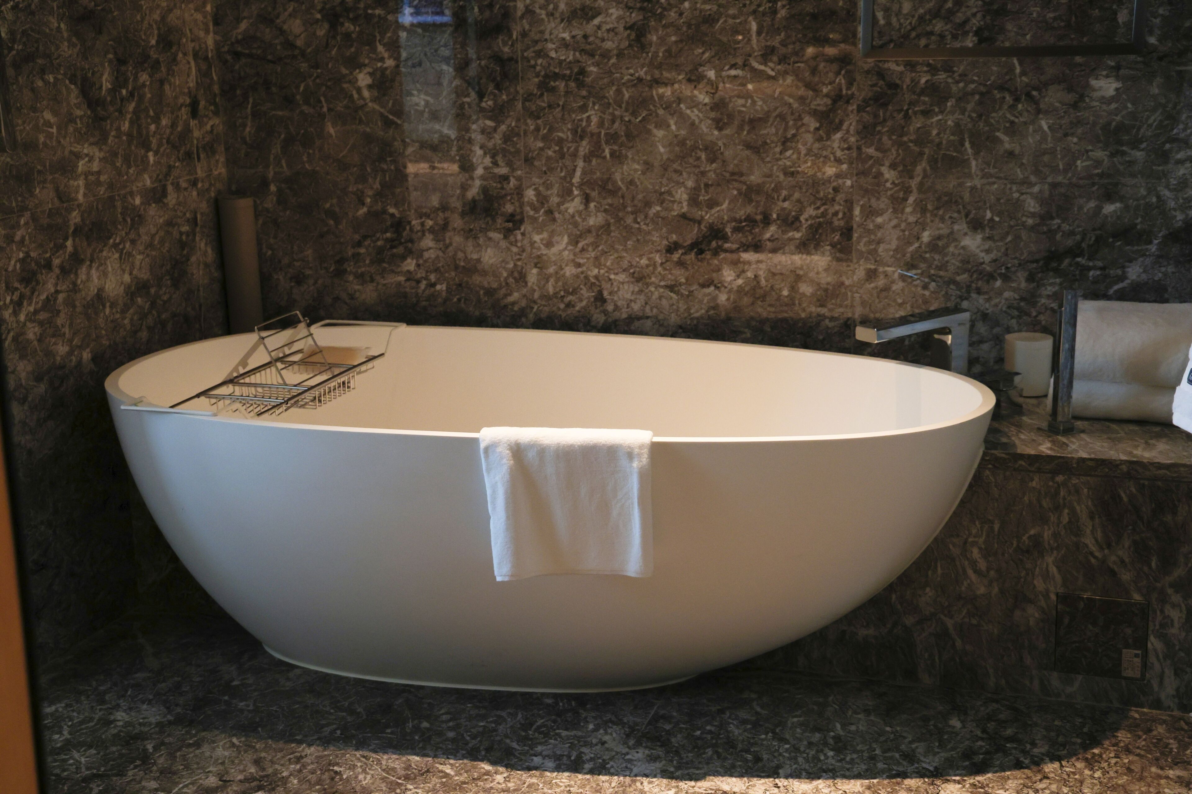 A modern bathroom with a freestanding bathtub, marble walls, and a towel hanging on the tub.