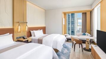 Habitación de hotel con dos camas, un escritorio, una silla, un televisor y un amplio ventanal con vista a la ciudad.