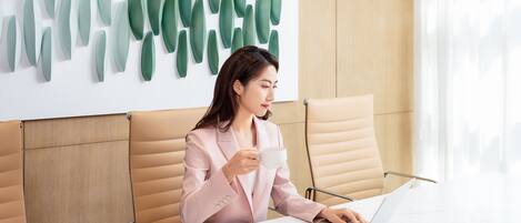 A person in a pink blazer at a table with a laptop, a white mug, and a spoon on a plate.