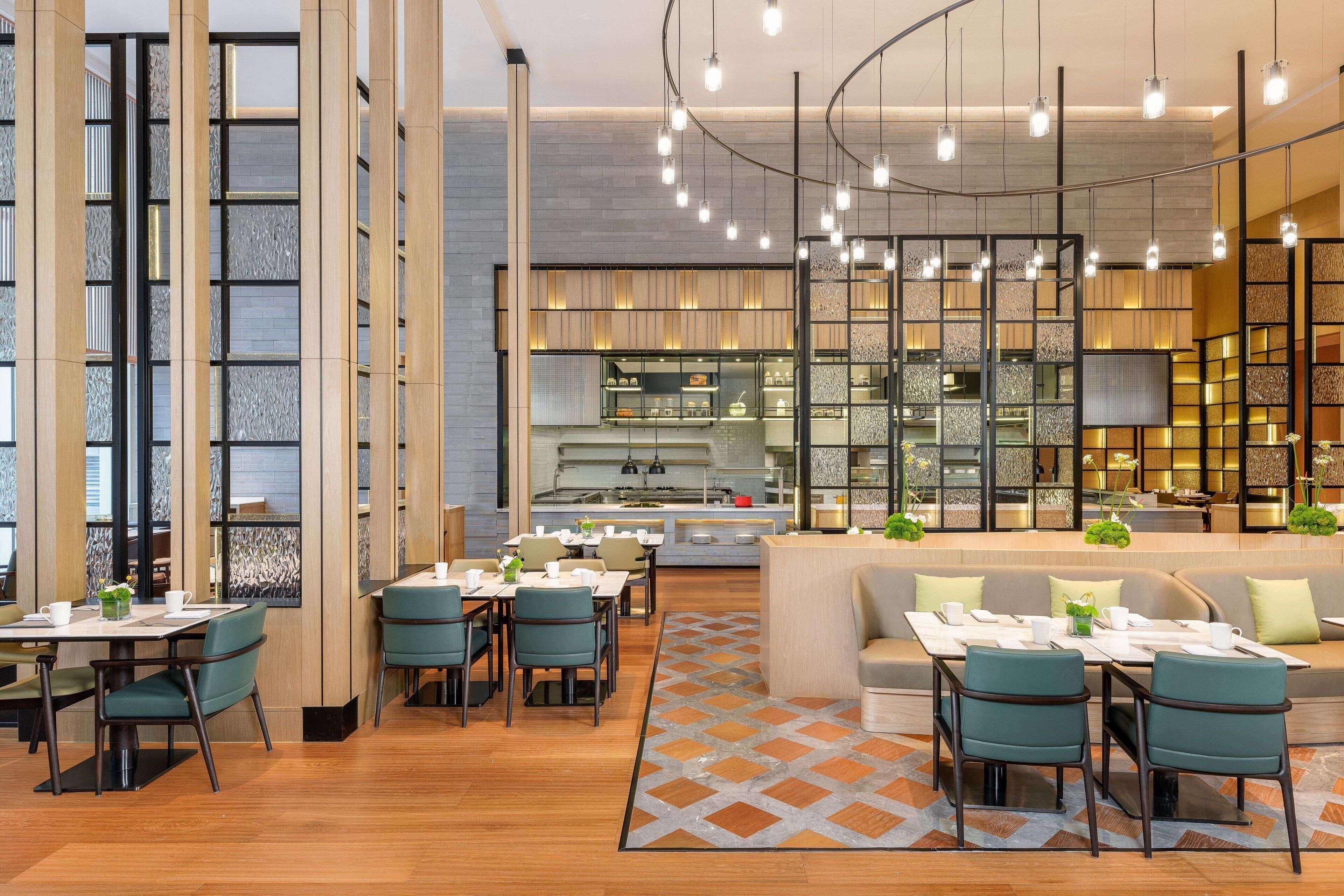 A modern restaurant with a central bar, seating areas, and a kitchen in the background.
