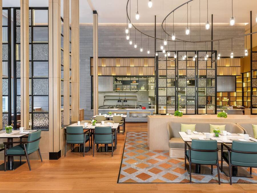 A modern restaurant with a central bar, seating areas, and a kitchen in the background.