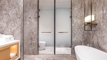 A modern bathroom with a marble floor, a white bathtub, a glass-enclosed shower, and a wooden vanity with a mirror.