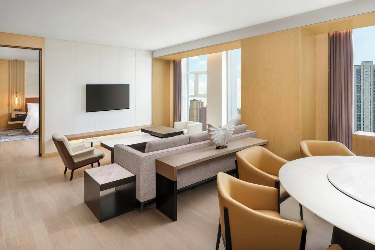 Una habitación de hotel moderna con sofá, sillas, una mesa de comedor y televisor.