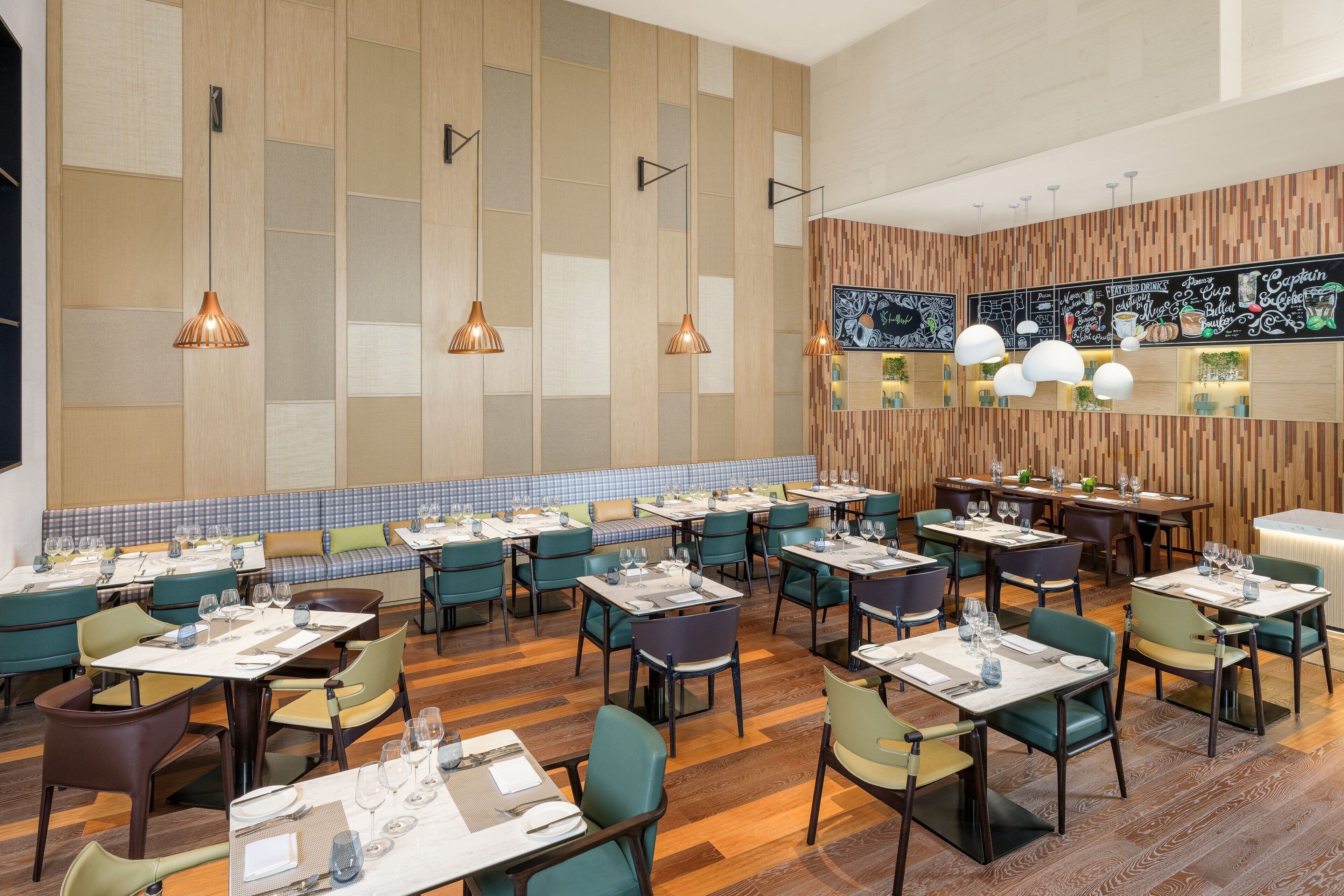 Un restaurant doté de nombreuses tables et chaises, de murs recouverts de panneaux de bois et de luminaires suspendus.