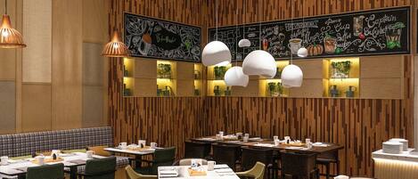 A modern restaurant interior with wooden panel walls, multiple dining tables, and pendant lighting.