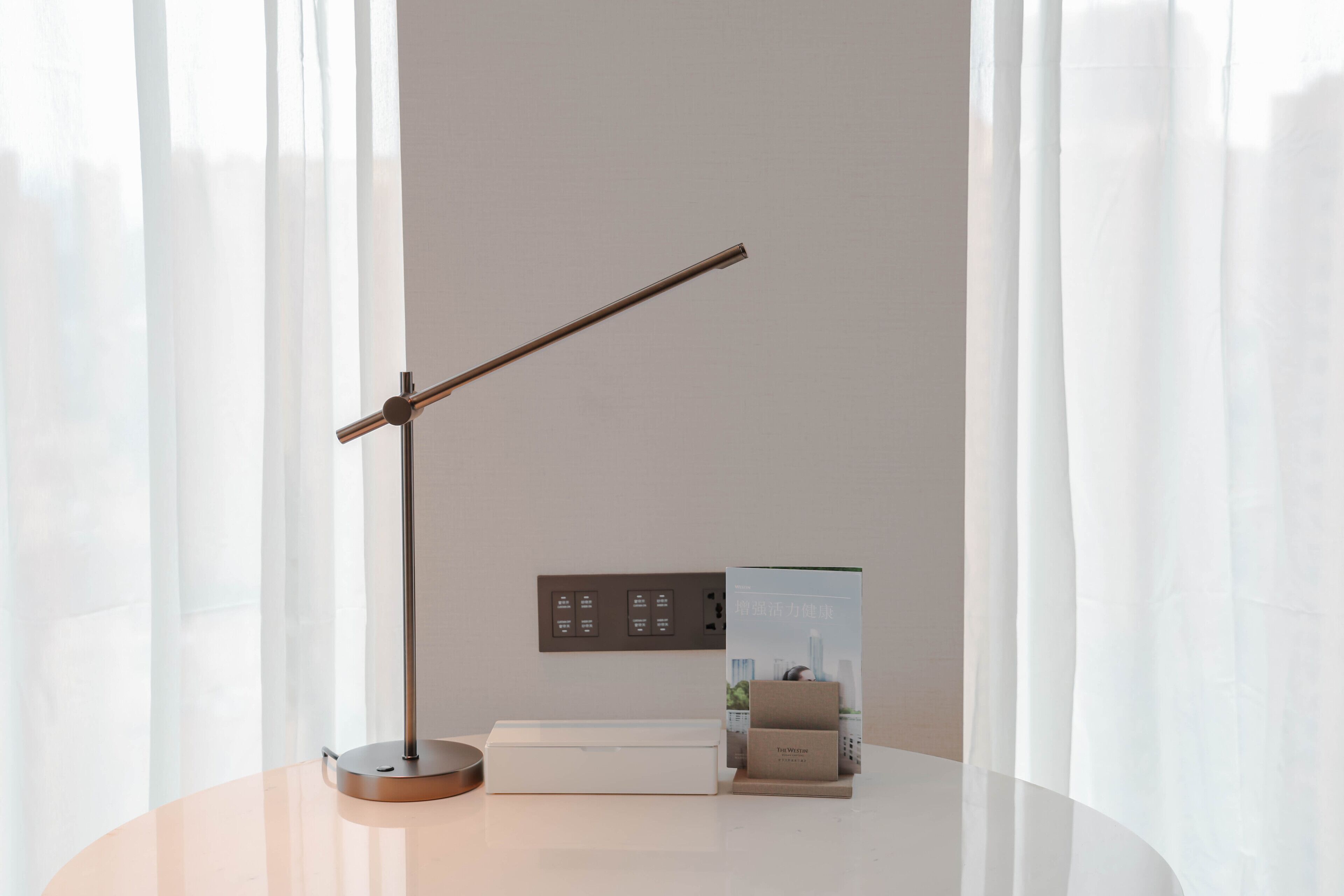 A modern desk with a lamp, a box, and a small display unit against a plain wall.
