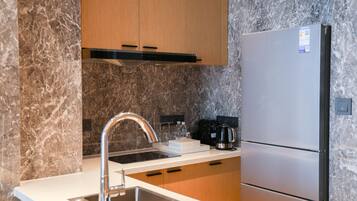 A modern kitchen with a stainless steel refrigerator, a built-in oven, and a marble backsplash.