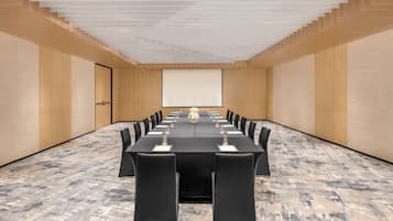 A conference room with a long table, chairs, a projector screen, and a carpeted floor.