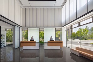 Un área de recepción moderna con dos recepcionistas en mostradores, ventanas amplias y un suelo limpio y reflectante.
