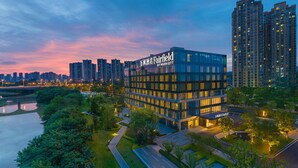 Un hotel moderno con fachada de vidrio, rodeado de edificios altos y un río.