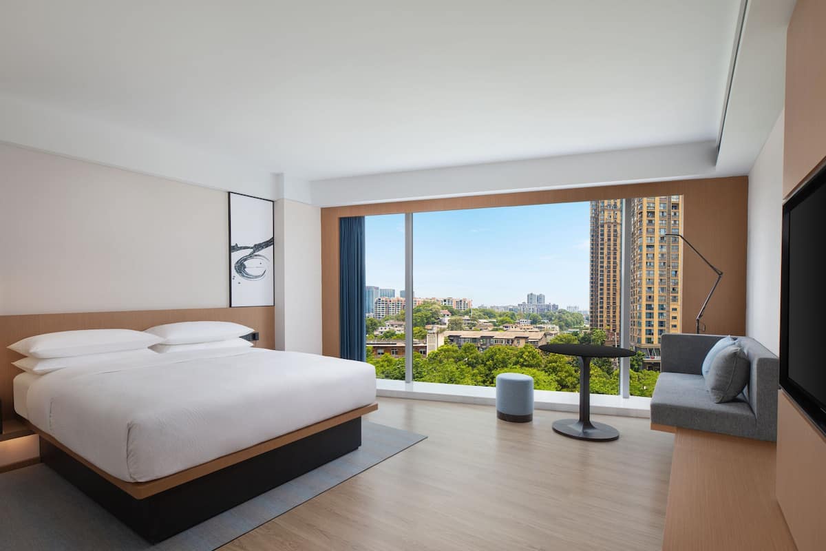 A modern hotel room with a large bed, a sofa, a TV, and a view of the city.