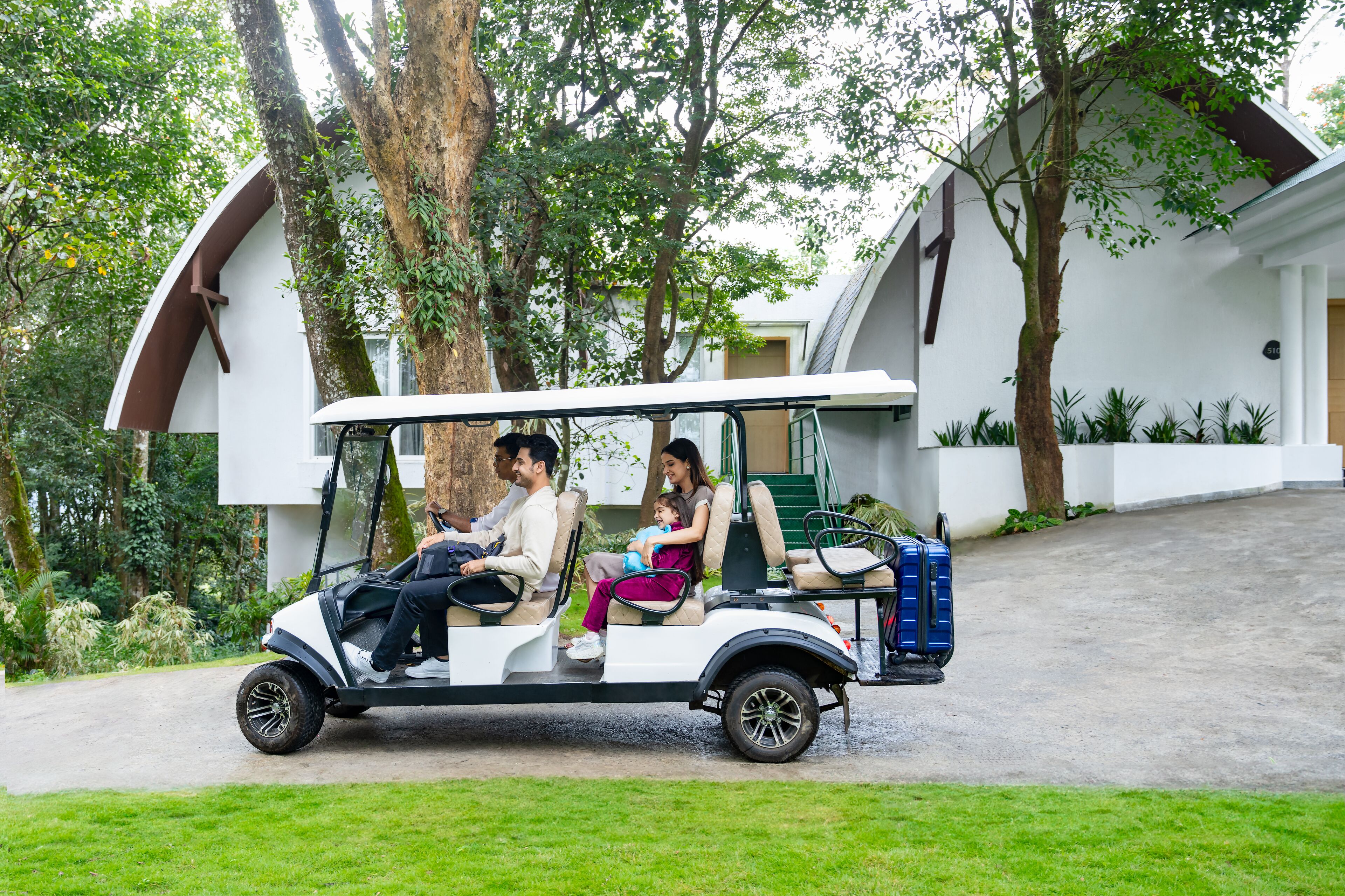 A golf cart with passengers, parked in front of a building with a white exterior and a sloped roof.