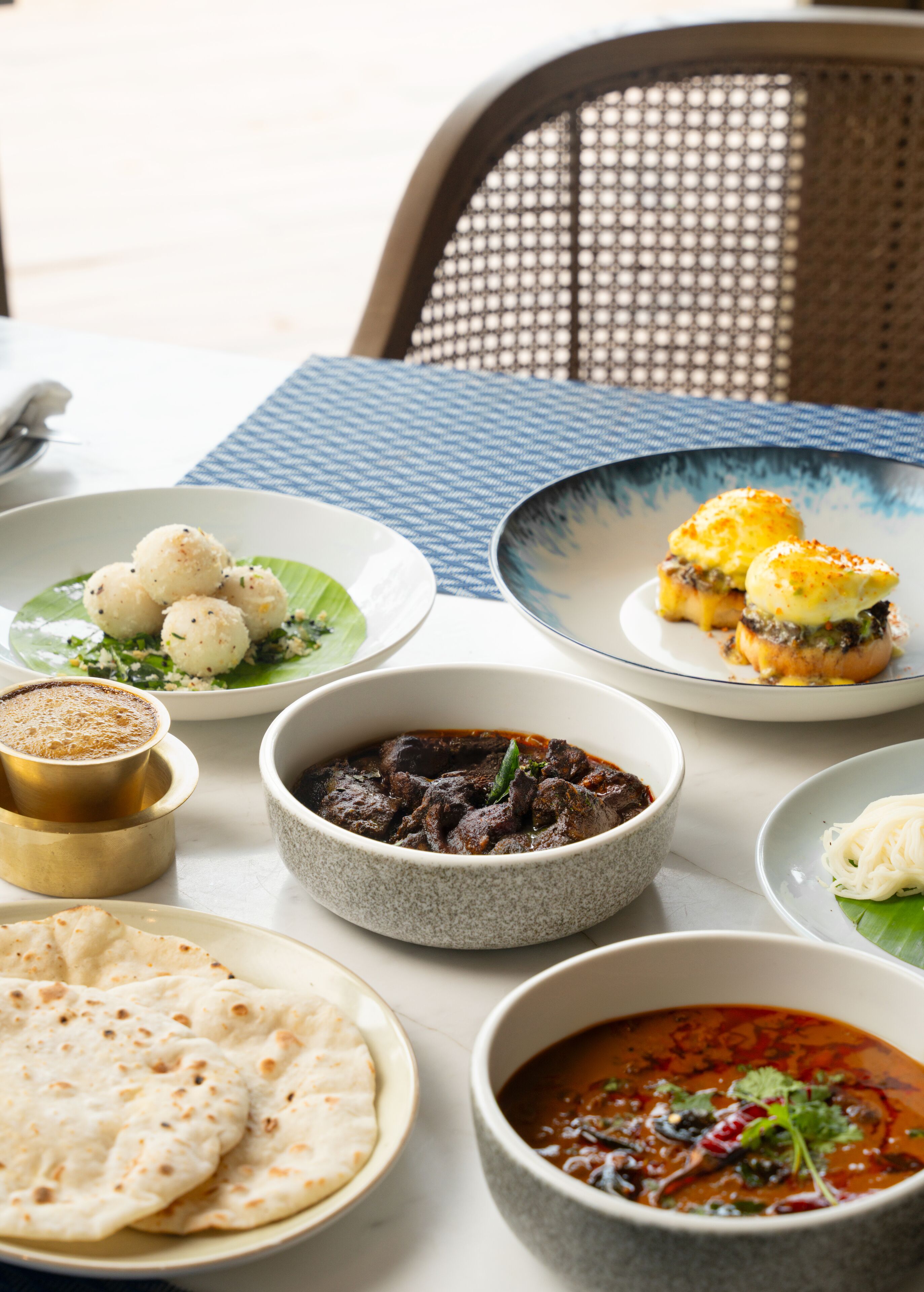 A table with various dishes, including flatbreads, curries, and a dessert.